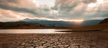 A cracked surface in foreground with a water body in the background along with mountains for Climate Change
