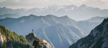 A person standing with a view of mountains in front A person standing with a view of mountains in front