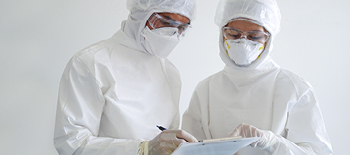 Two researchers working and looking down in their protective gear