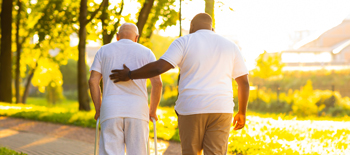 Older man being supported in his walk in park  Older man being supported in his walk in park