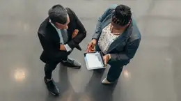 Two colleagues standing together and looking at an electronic tablet screen